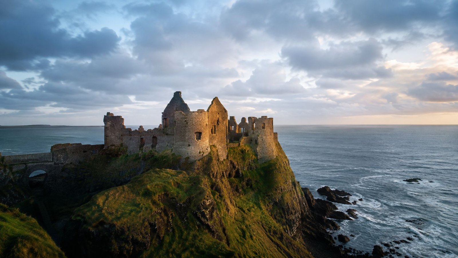 A scenic view of the ruins of Dunluce Castle perched on a cliffside by the Irish Sea.